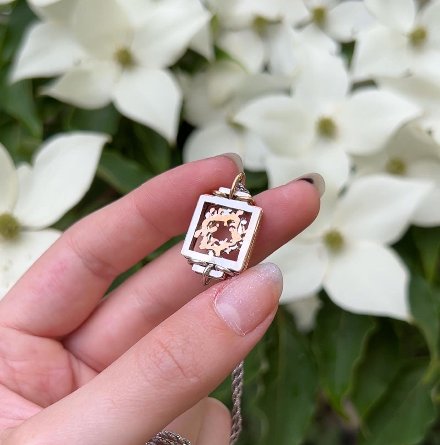 Beautiful small pendant, made of layers of sheet metal coming to form an abstract flower wreath. Released 2023 (currently not sold), Background of green leaves and white dogwood flowers