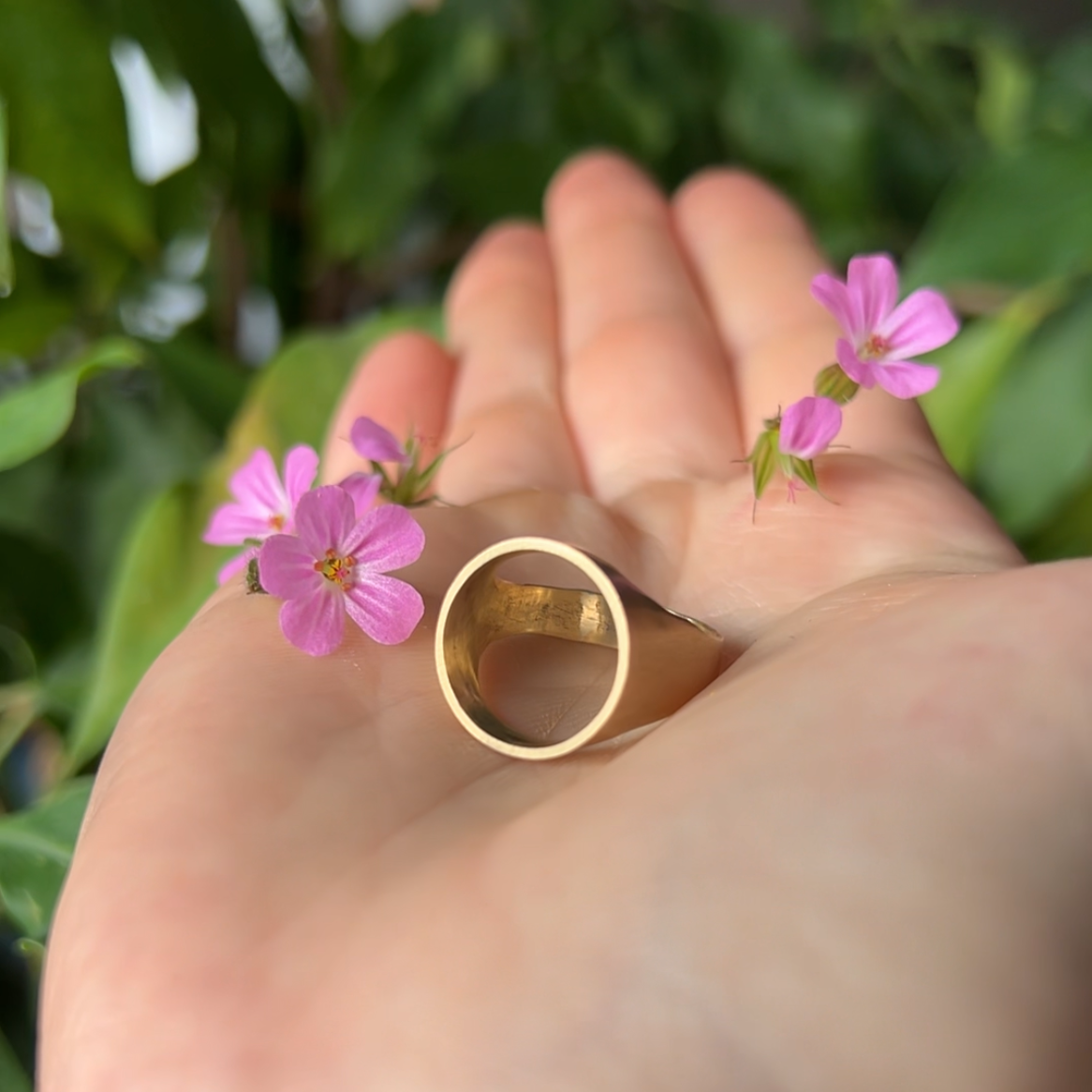 Brass Signet Ring sitting in palm surrounded by pink flowers